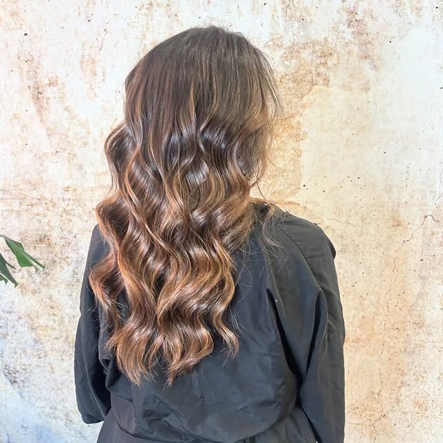 Mujer con cabello castaño largo y ondulado, que cae en cascada sobre un top negro