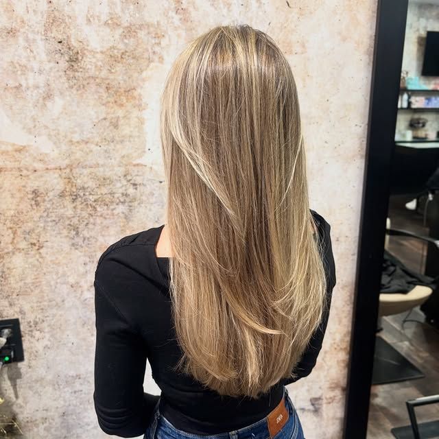 Cabello rubio con reflejos, corte a capas. Persona con camisa negra, de pie en un salón de belleza.