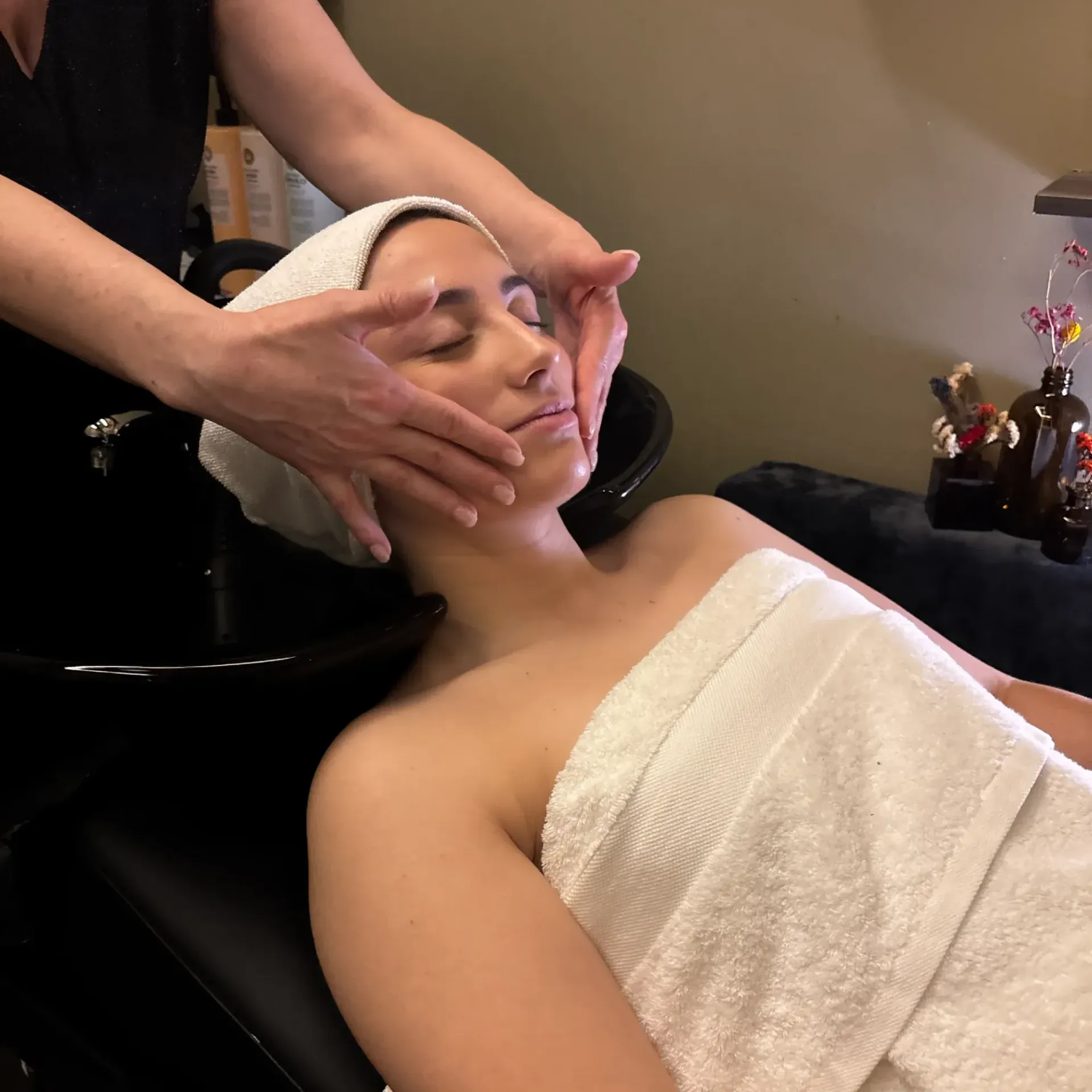 Un estilista peina a una clienta en un salón. La clienta mira su tableta mientras otro estilista le da consejos en el espejo.