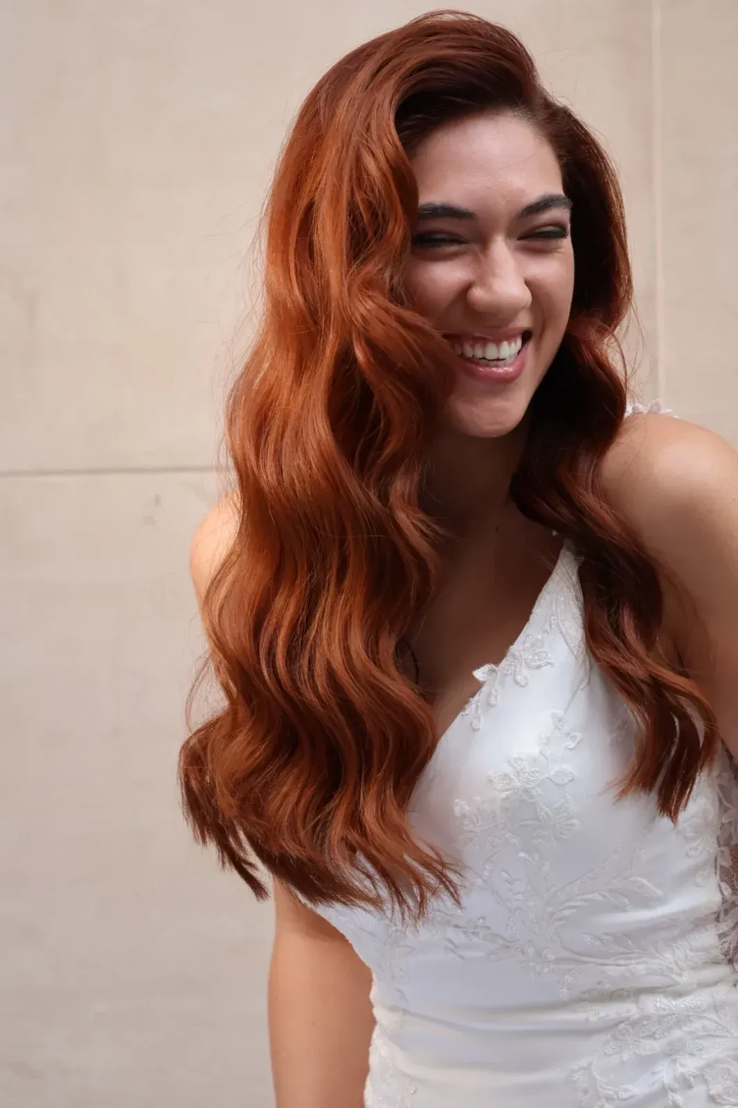 Mujer con cabello castaño largo y ondulado, que lleva una pinza para el cabello con flores blancas; vista desde atrás.