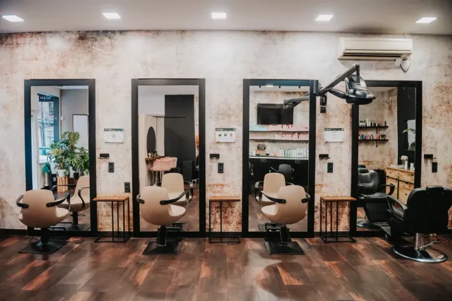 Mujer con cabello rubio largo, ondulado y ombré, con falda de mezclilla, parada frente a una pared texturizada.