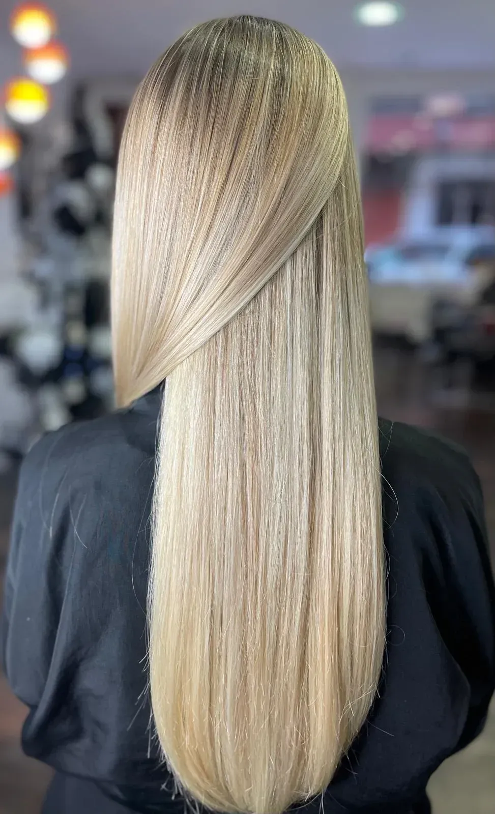 Cabello rubio largo y liso con reflejos sutiles, peinado sobre un hombro.