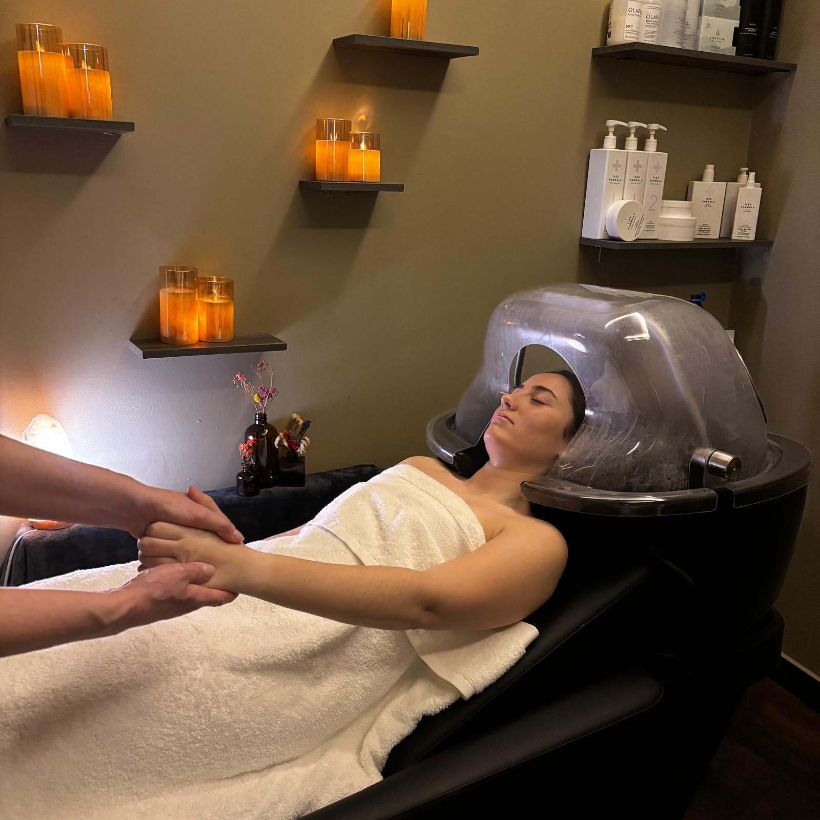 Un estilista peina a una clienta en un salón. La clienta mira su tableta mientras otro estilista le da consejos en el espejo.