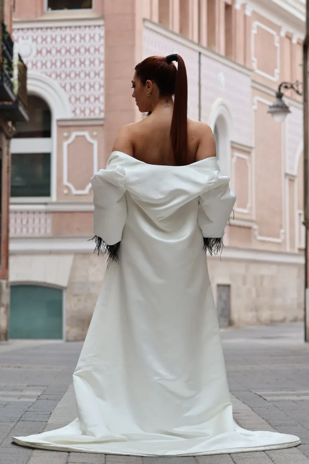 Mujer con vestido blanco, de espaldas a la cámara, en un callejón adoquinado