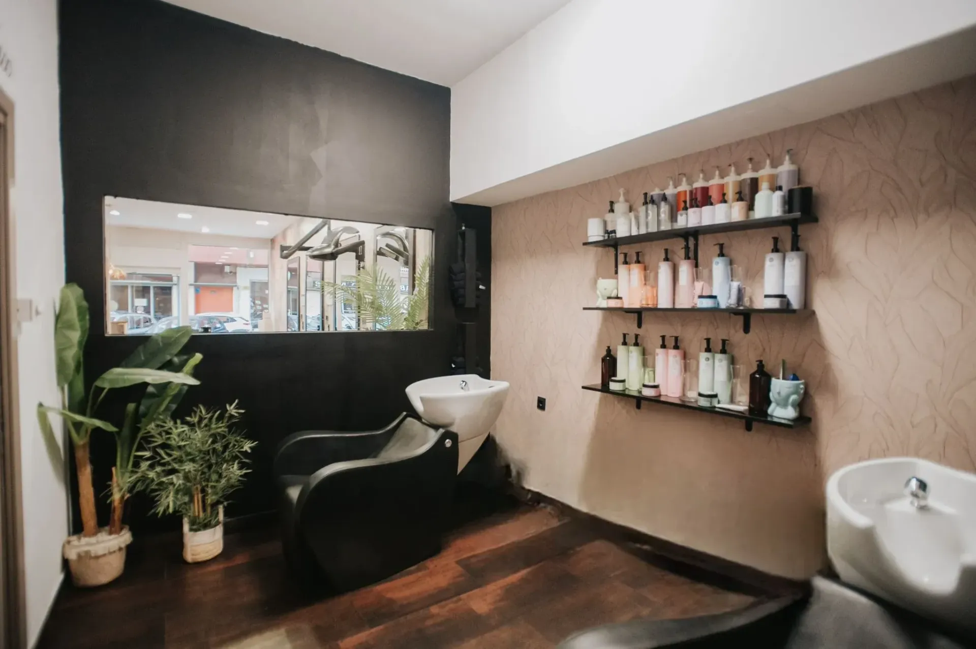 Interior de peluquería con silla de peluquería, lavabos, estantes de productos y un espejo grande.