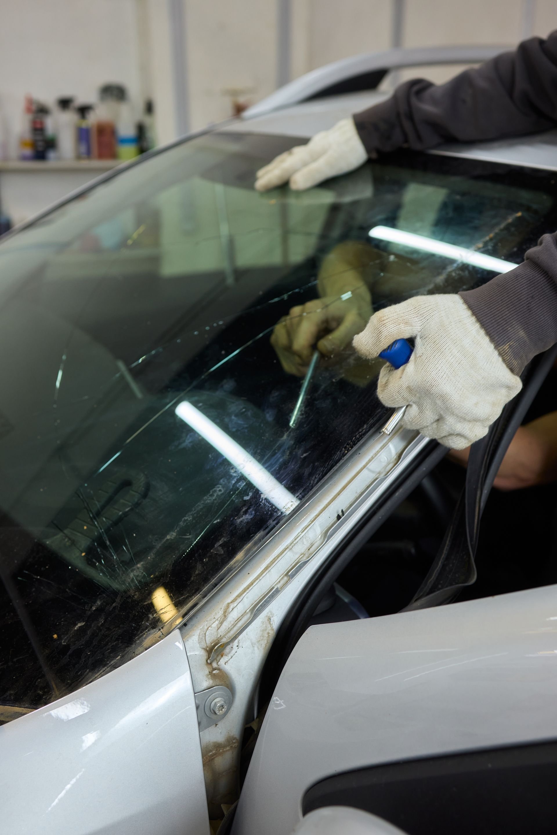 Une personne portant des gants utilise un outil pour retirer un pare-brise de voiture dans un atelier de réparation.
