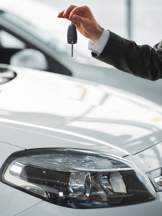 Main tenant des clés de voiture au-dessus d'une voiture blanche dans une salle d'exposition.