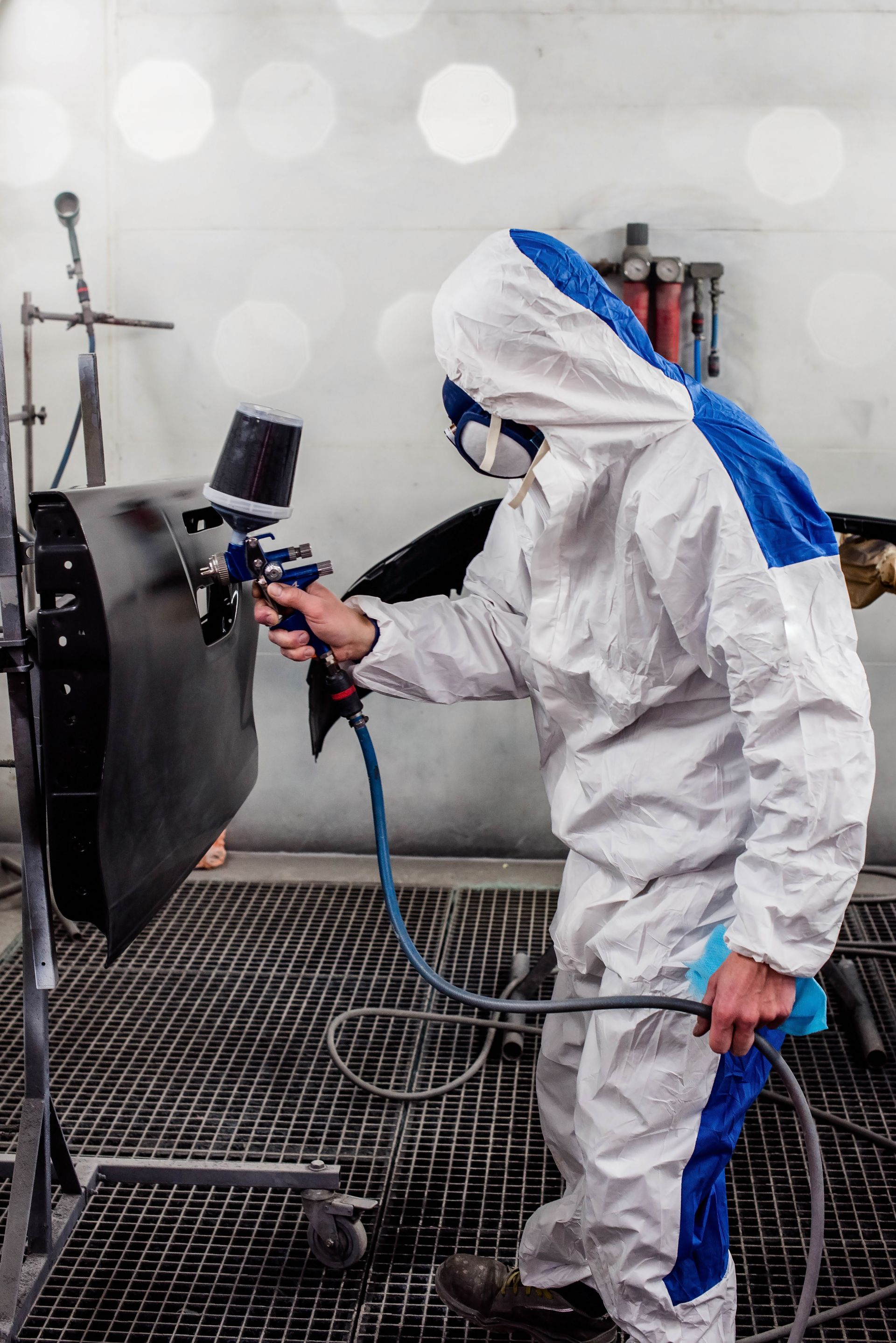 Une personne en combinaison de protection peint une portière de voiture avec un pistolet pulvérisateur.