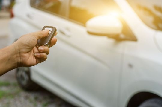 Main tenant un porte-clés de voiture, déverrouillant une voiture blanche au soleil.