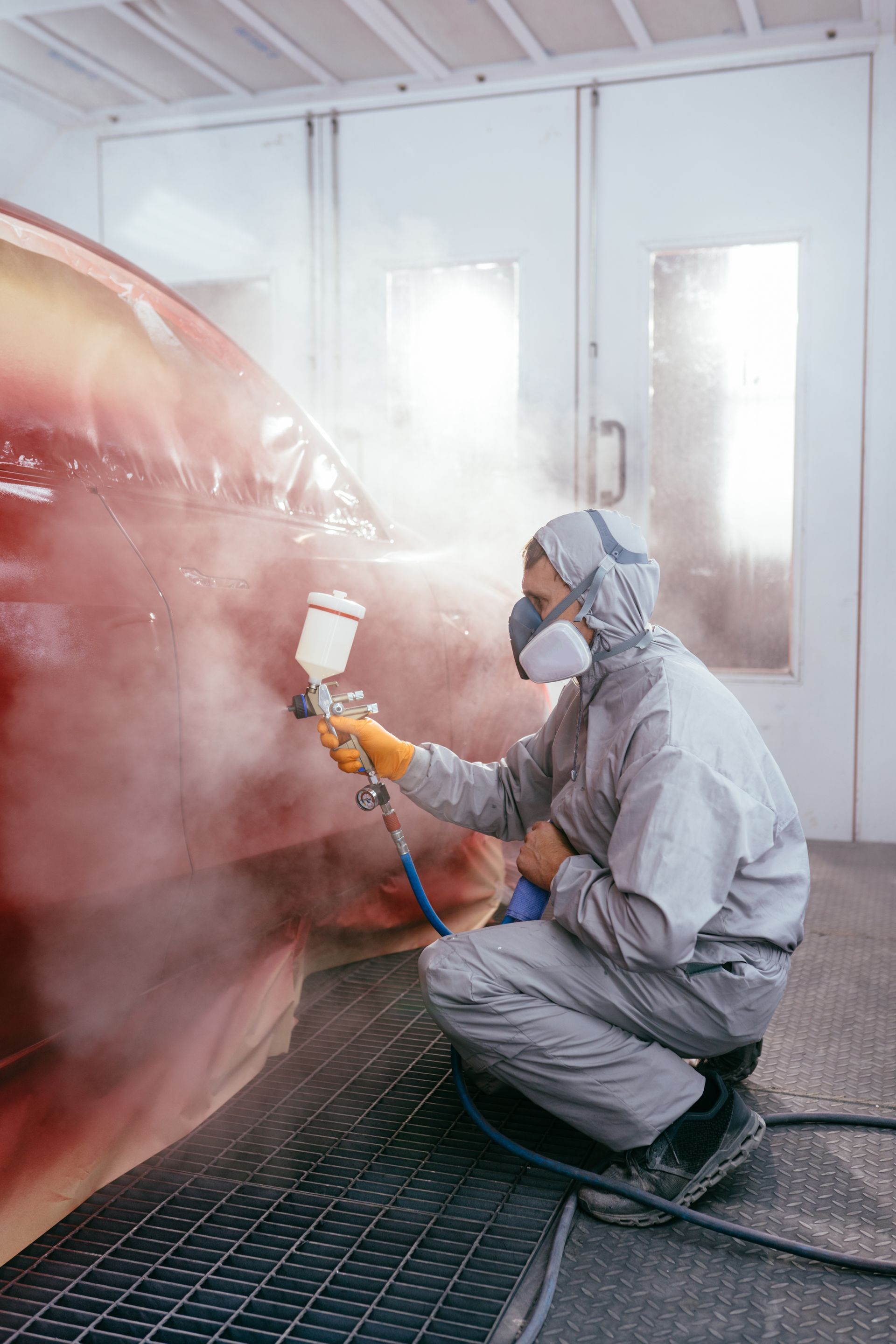 Une personne en combinaison de protection pulvérise de la peinture sur une voiture dans une cabine de peinture.