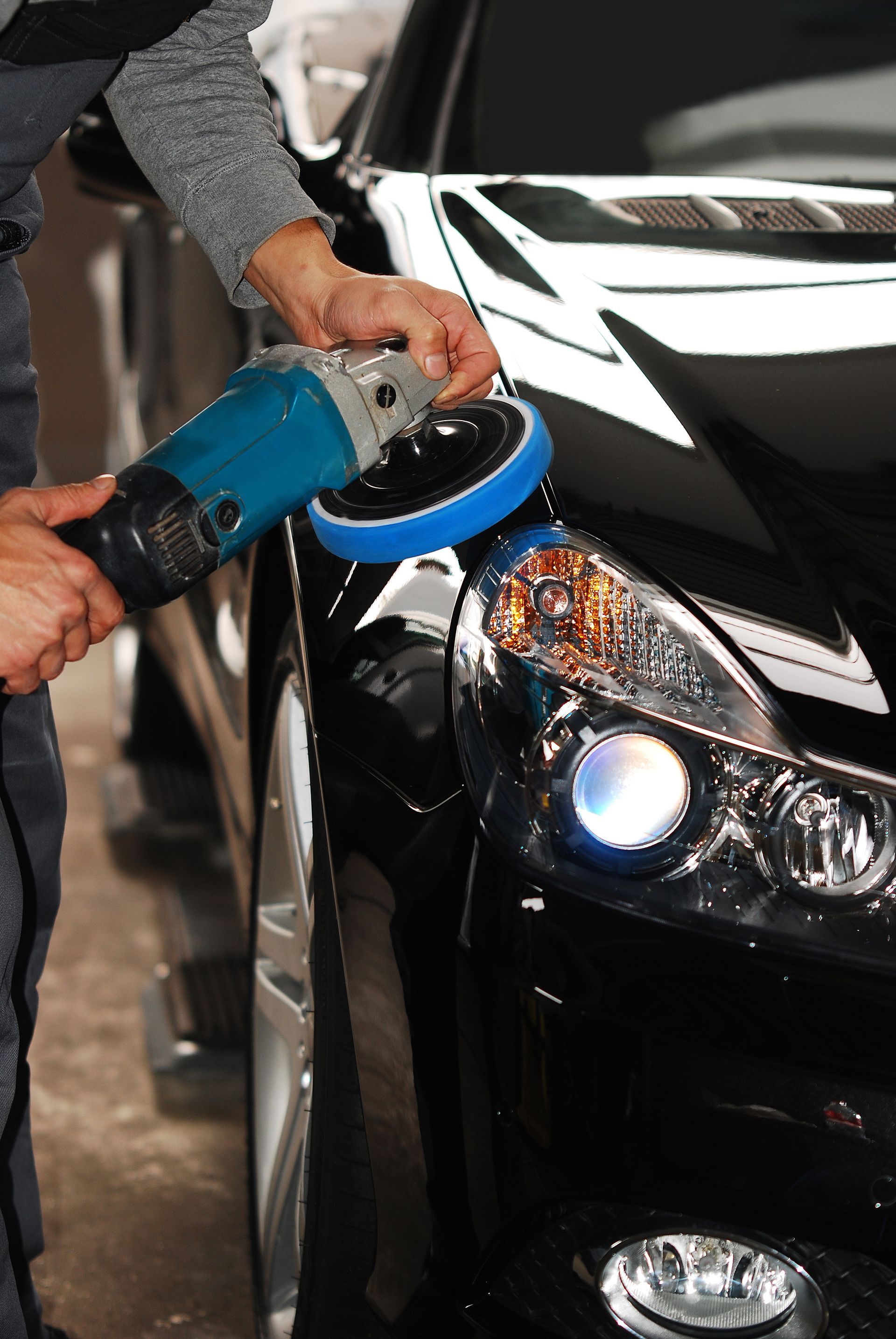 Personne polissant un phare de voiture noir avec une polisseuse électrique bleue.