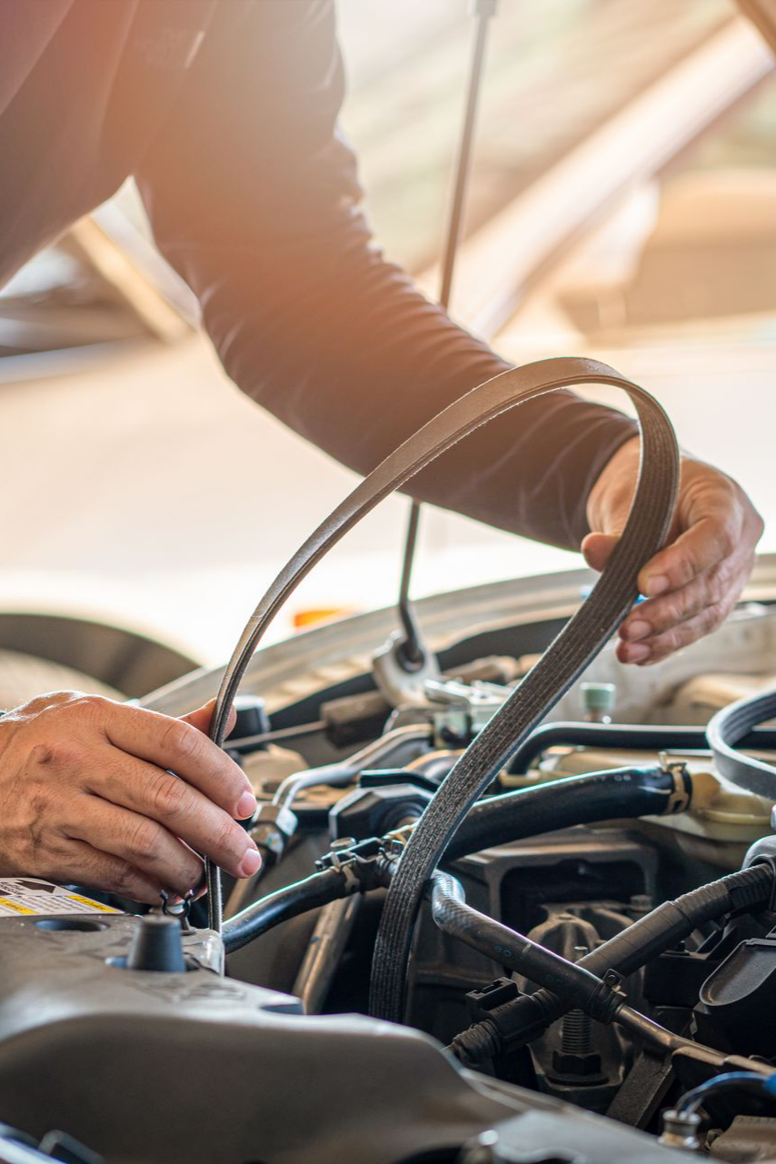 Une personne tenant une courroie noire près d'un moteur de voiture, en préparation d'une réparation.
