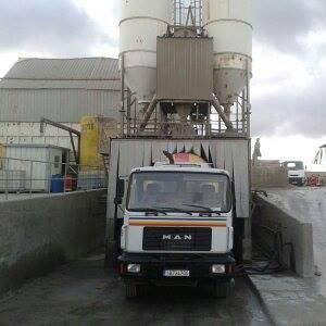 Un camión de carga está estacionado frente a una planta de hormigón.