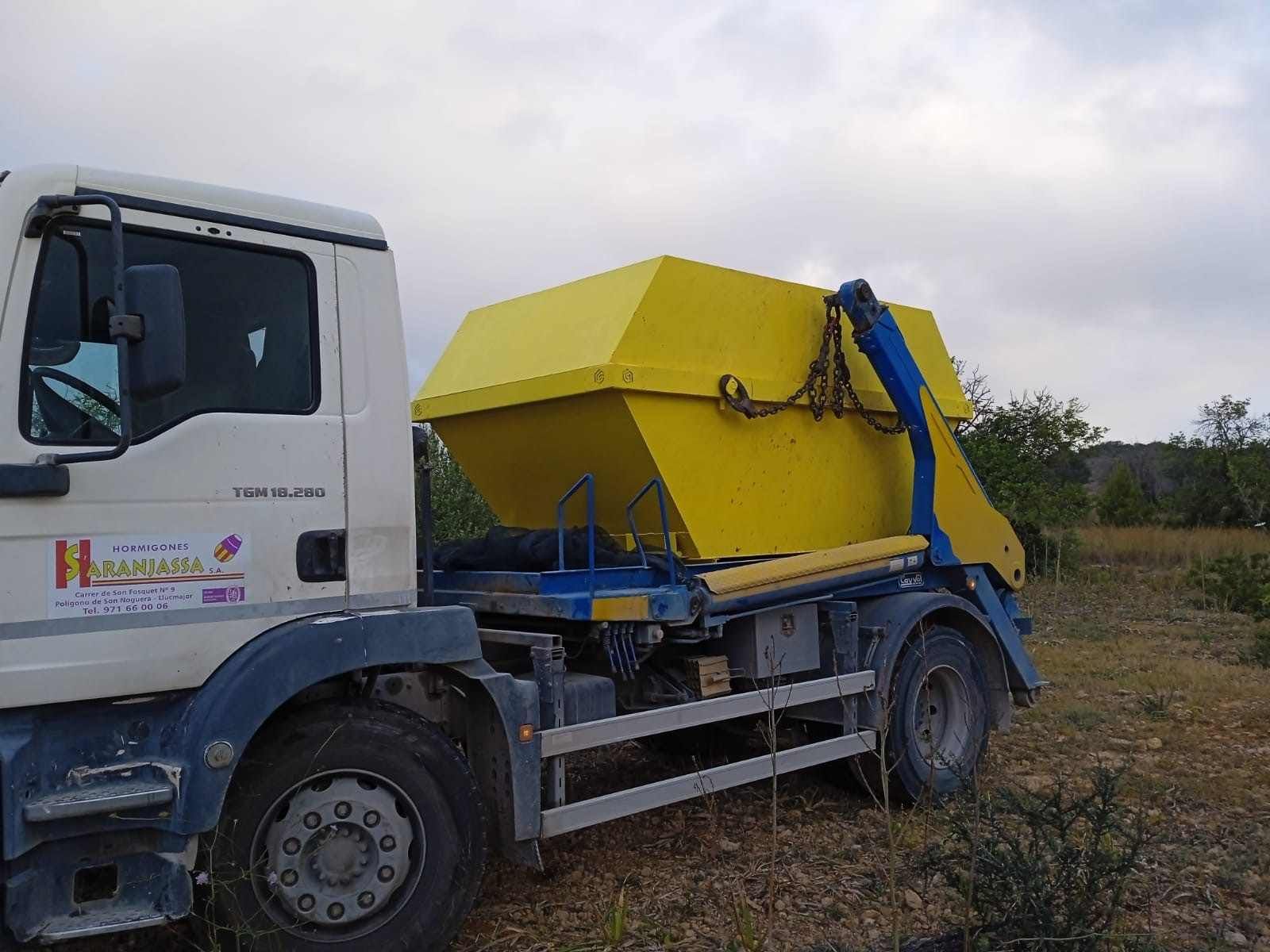 Un camión volquete con un contenedor amarillo en la parte trasera está estacionado en un campo.