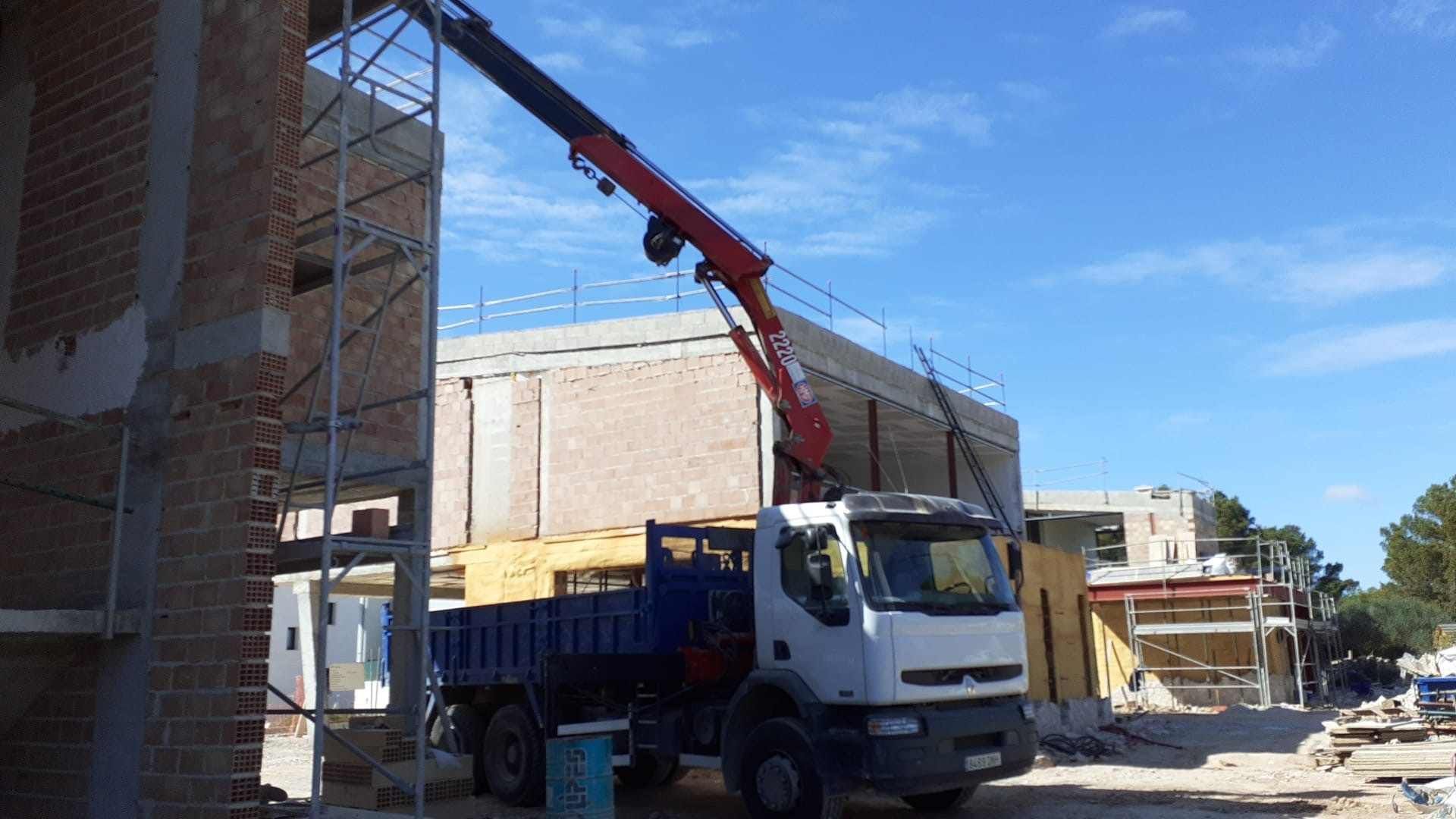 Un camión con una grúa acoplada está estacionado delante de un edificio en construcción.