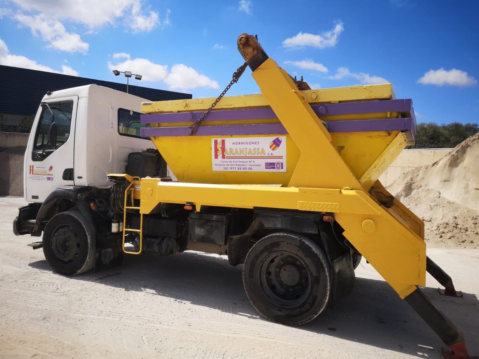 Un camión volquete amarillo y morado está estacionado en un camino de tierra.