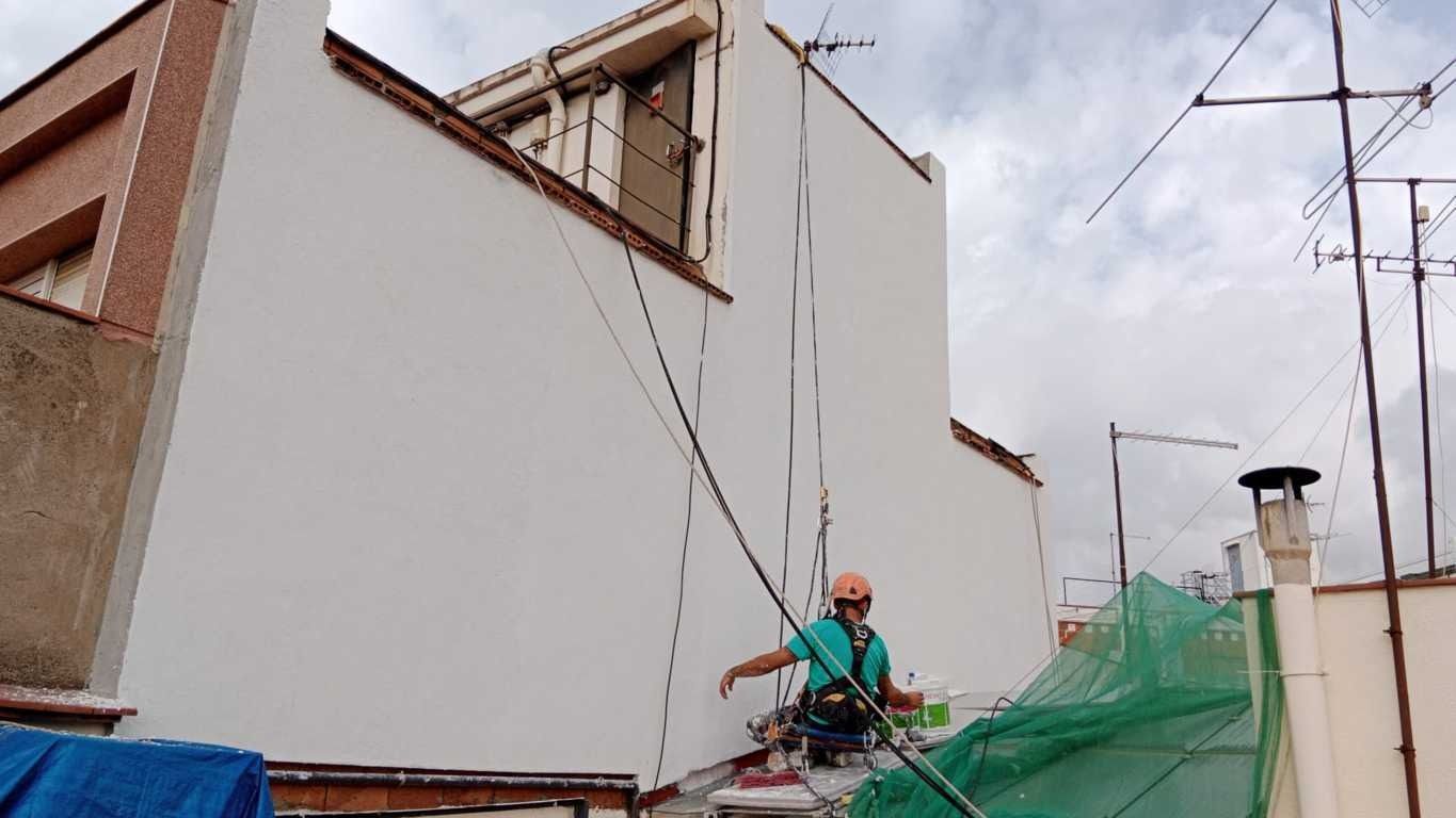Un hombre está pintando el costado de un edificio con una cuerda.