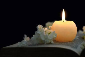 Eine entzündete Kerze und Blumen liegen auf einem Blatt mit Text.