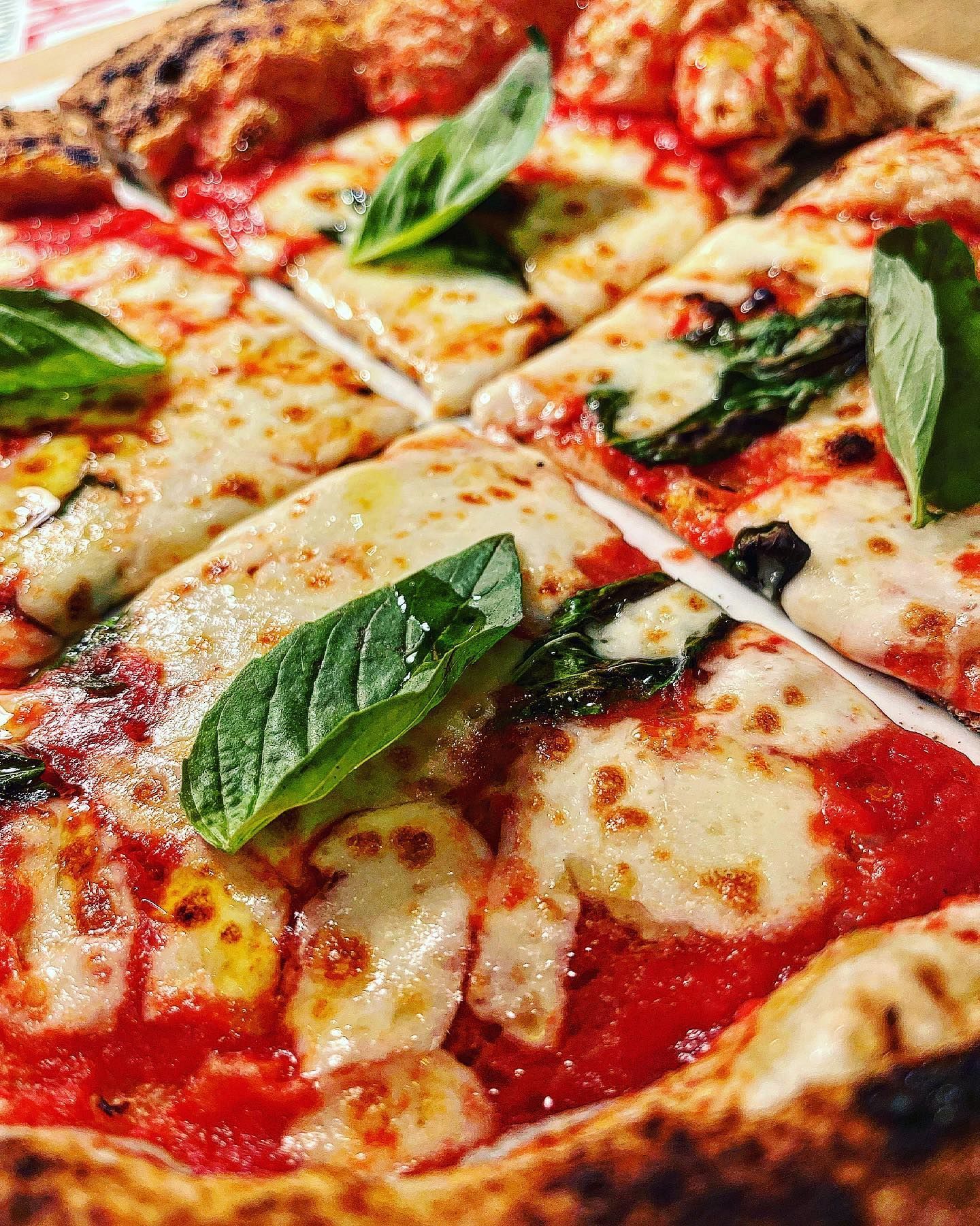 Gros plan sur une pizza avec sauce tomate, fromage fondu et feuilles de basilic frais, coupée en tranches et prête à être dégustée.