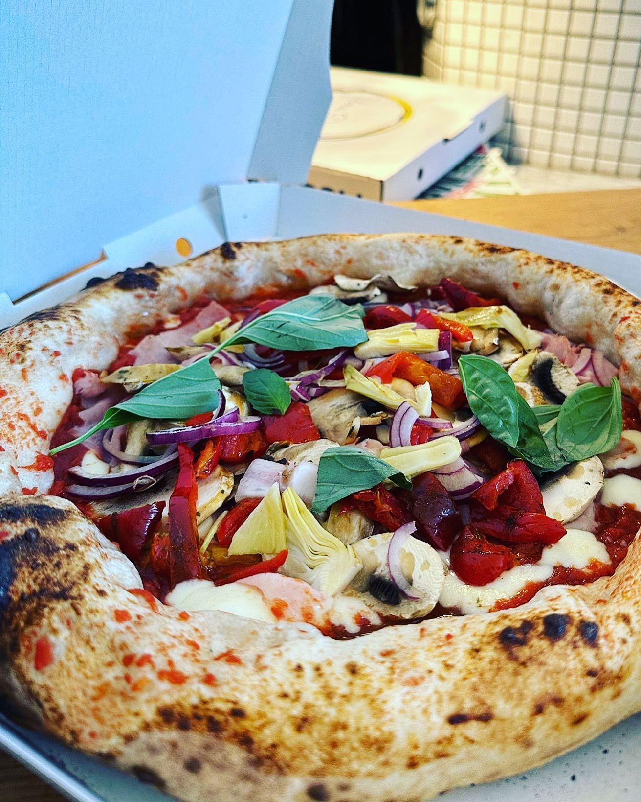 Pizza à la sauce tomate, aux légumes et au basilic, dans une boîte ouverte.