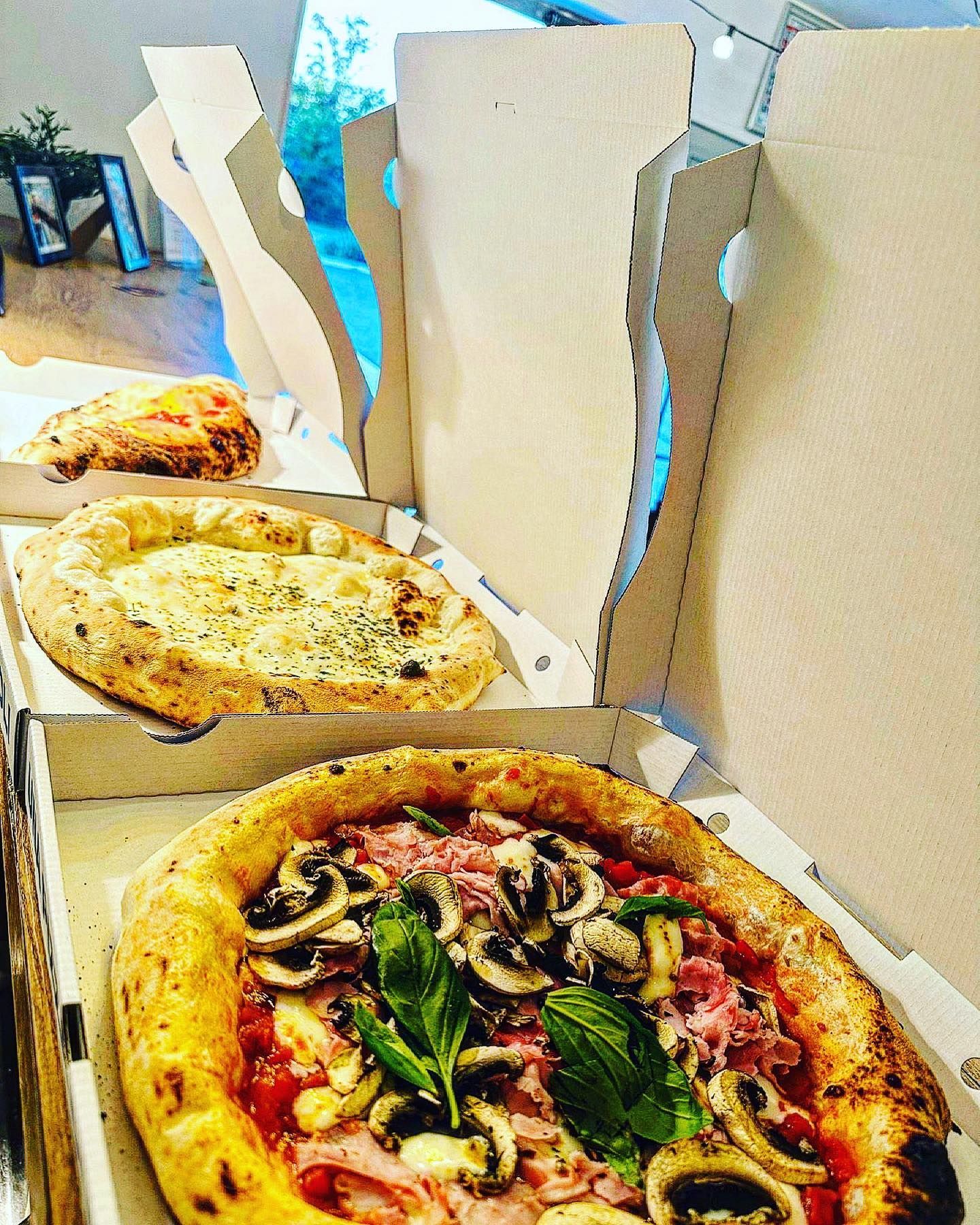 Des pizzas dans des boîtes ouvertes : une aux champignons, jambon et basilic ; une autre au fromage ; et une focaccia.