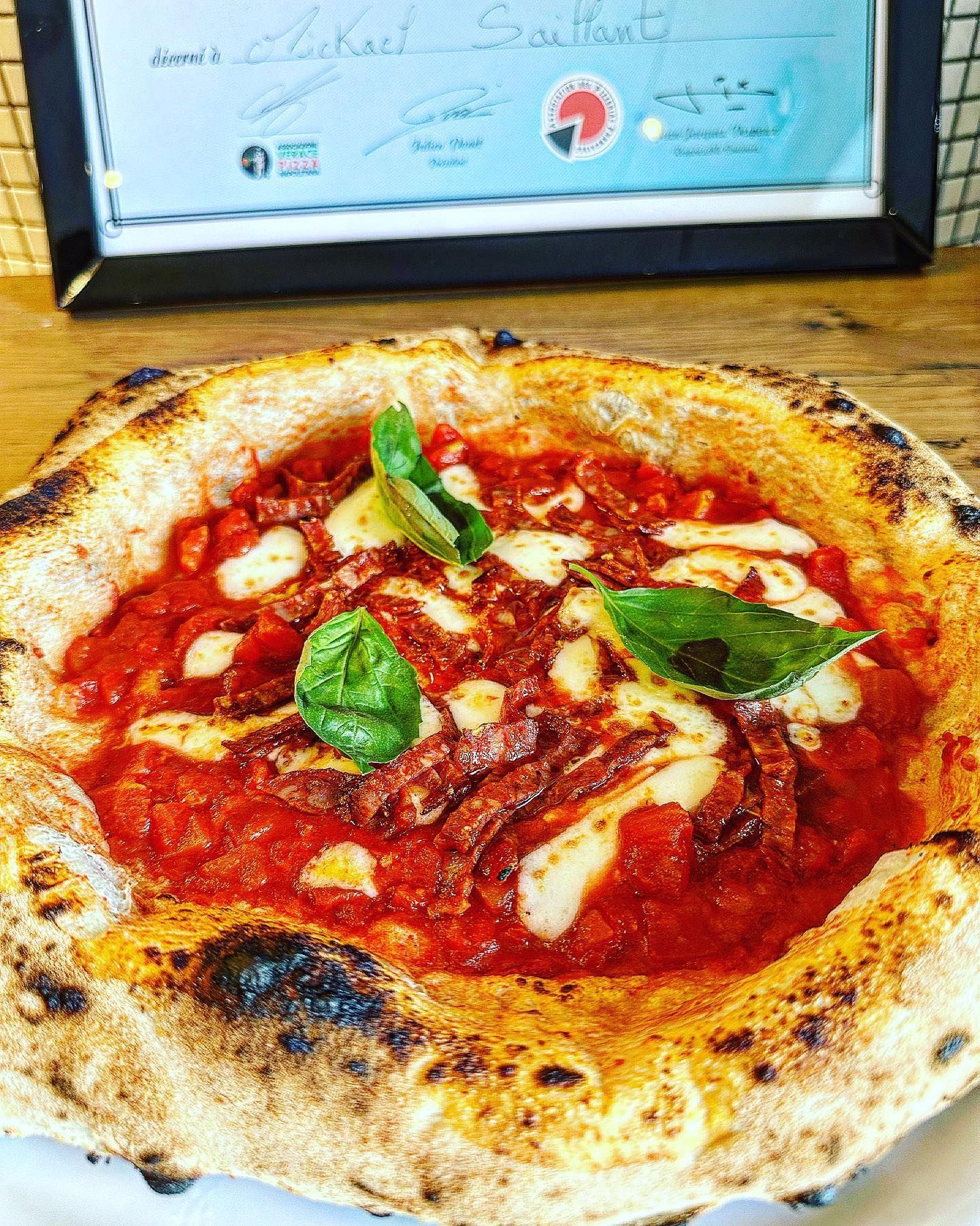 Gros plan sur une pizza à la sauce tomate, au fromage et aux garnitures, agrémentée de basilic, posée sur une surface en bois.