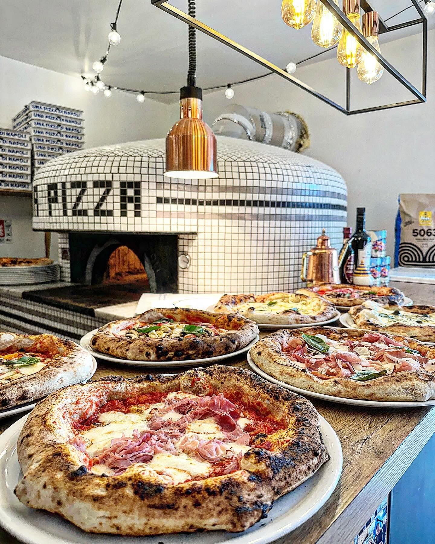 Pizzas sur un comptoir avec un four à bois en arrière-plan, ambiance restaurant italien.