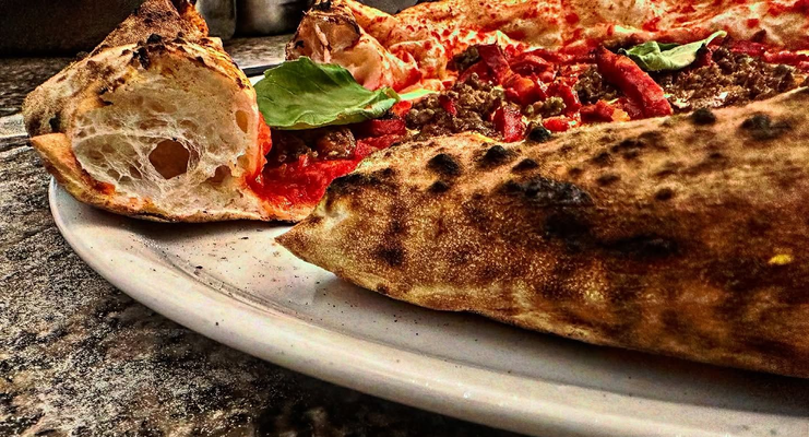 Gros plan sur une pizza dans une assiette blanche, montrant la texture de la croûte et les garnitures, notamment la sauce, la viande et le basilic.