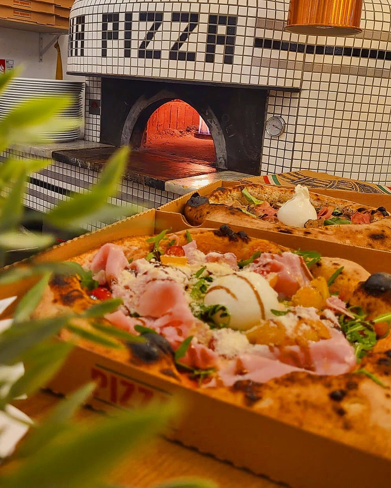 Des pizzas en boîte devant un four à bois. L'intérieur du four est d'une lueur orangée.