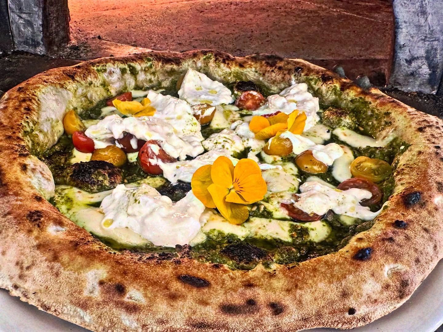 Pizza au pesto, tomates et fromage, devant un four à briques.