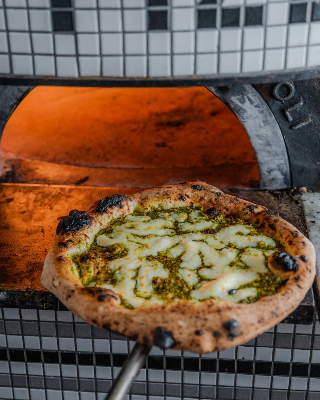 Une pizza au pesto et à la mozzarella est sortie du four à bois.