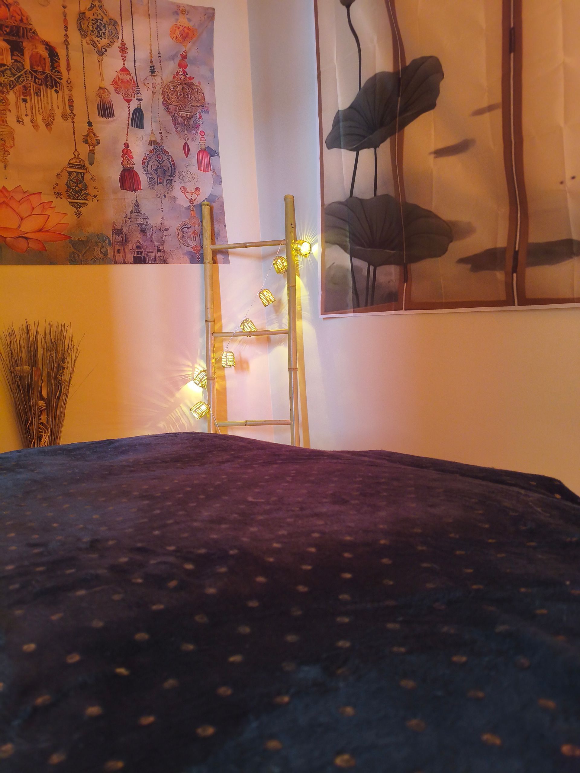 Une pièce confortable avec une couverture bleu foncé au premier plan, une échelle décorative en bois ornée d'une guirlande lumineuse et des tapisseries murales.