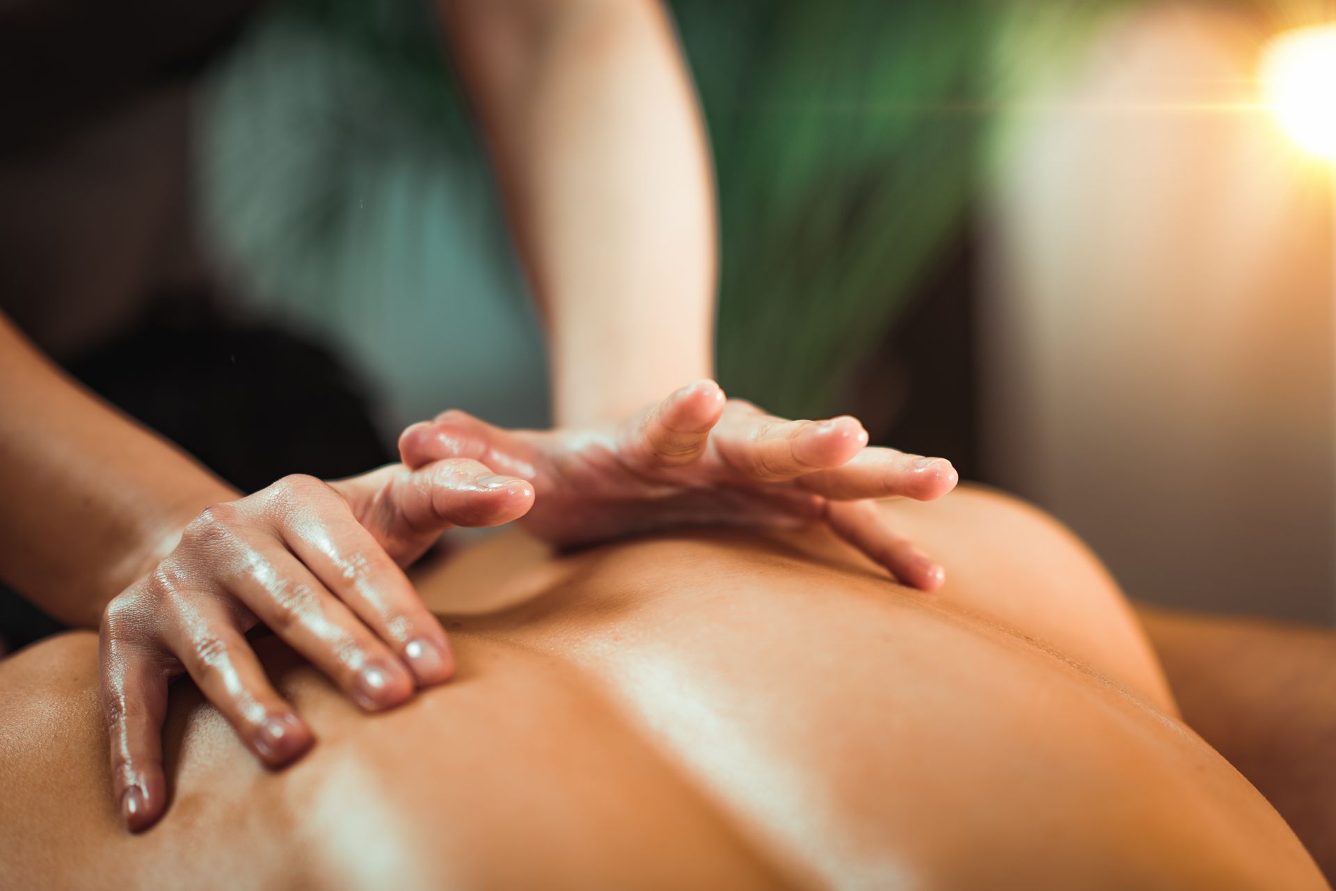 Gros plan sur des mains appliquant de l'huile lors d'un massage thérapeutique du dos d'une personne, dans une ambiance tamisée et chaleureuse.