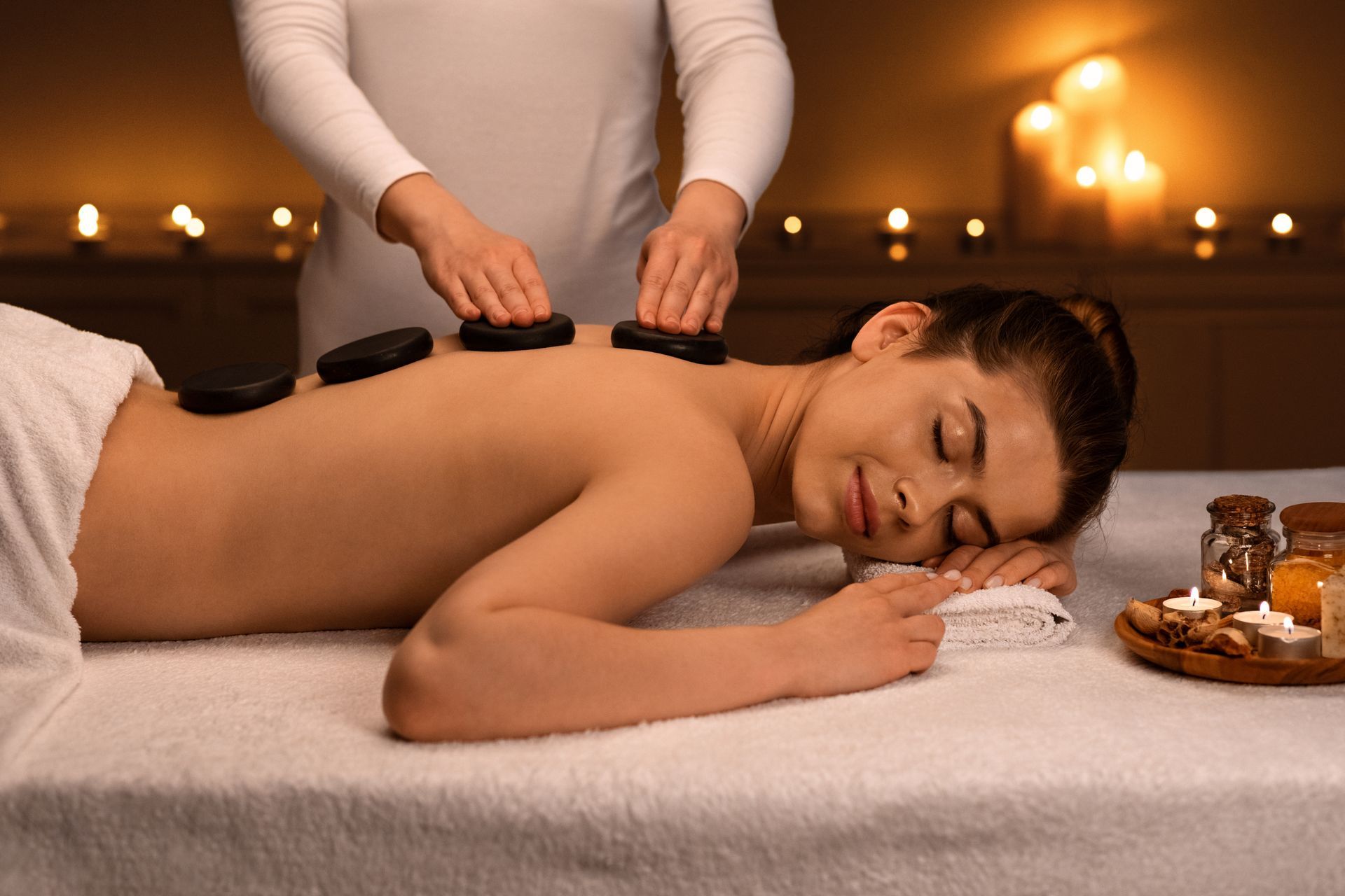 Une personne est allongée, détendue, sur une table de massage, et reçoit un massage aux pierres chaudes dans un spa à l'éclairage tamisé et éclairé à la bougie.
