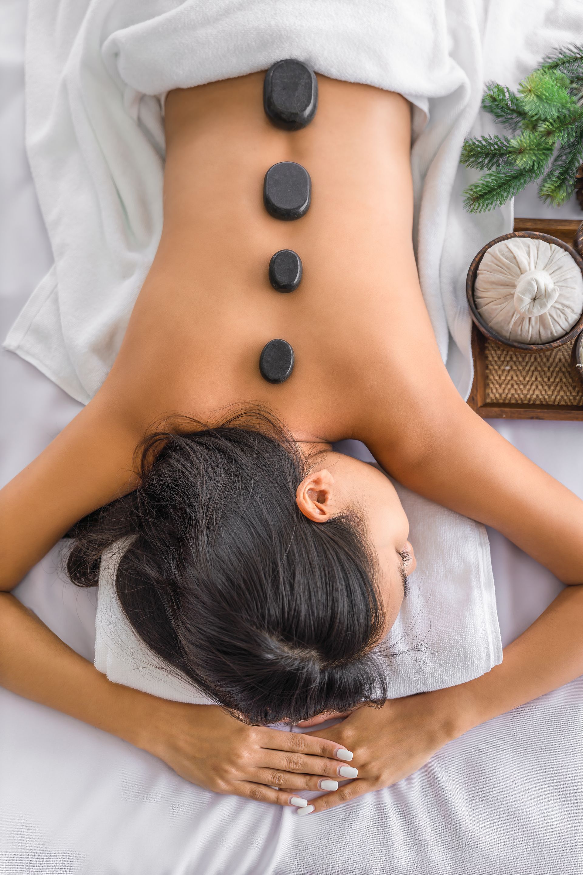 Une personne allongée sur le ventre sur une table de massage, quatre pierres lisses et sombres placées le long de sa colonne vertébrale.