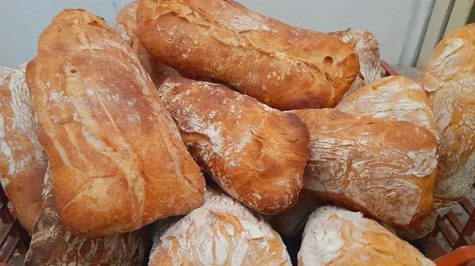 Montón de hogazas de pan crujientes y doradas, espolvoreadas con harina, en una cesta.