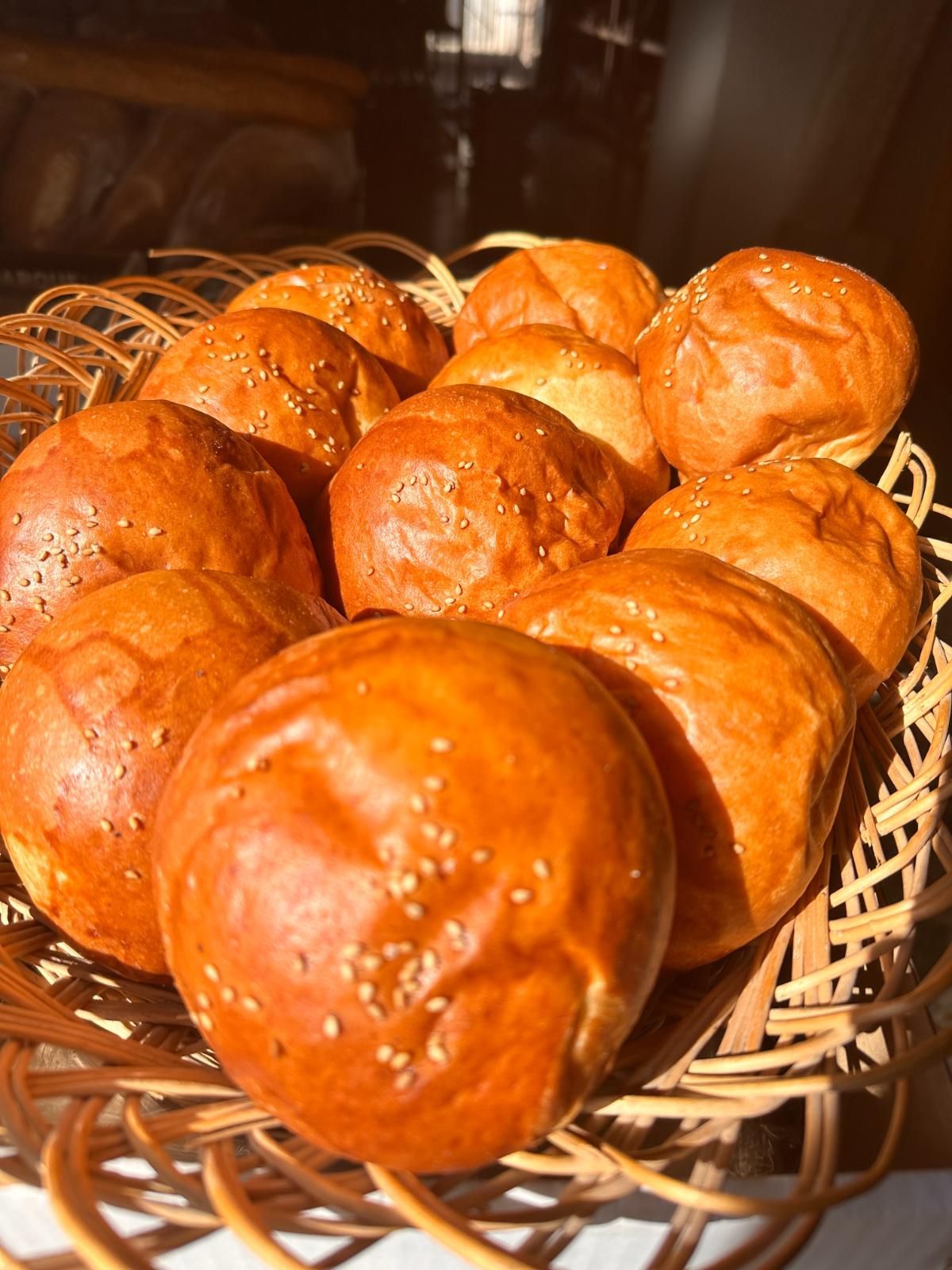 Panecillos dorados con semillas de sésamo en una cesta de mimbre, iluminados por la luz del sol.
