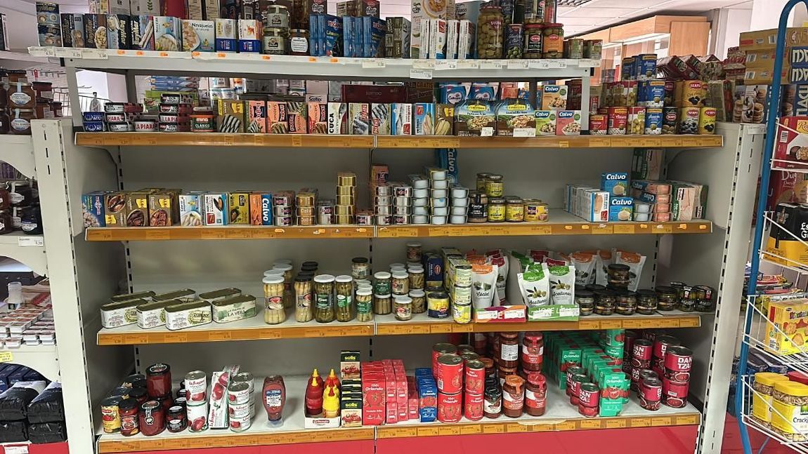 Estanterías repletas de diversos productos en una tienda; estanterías de color rojo y blanco.