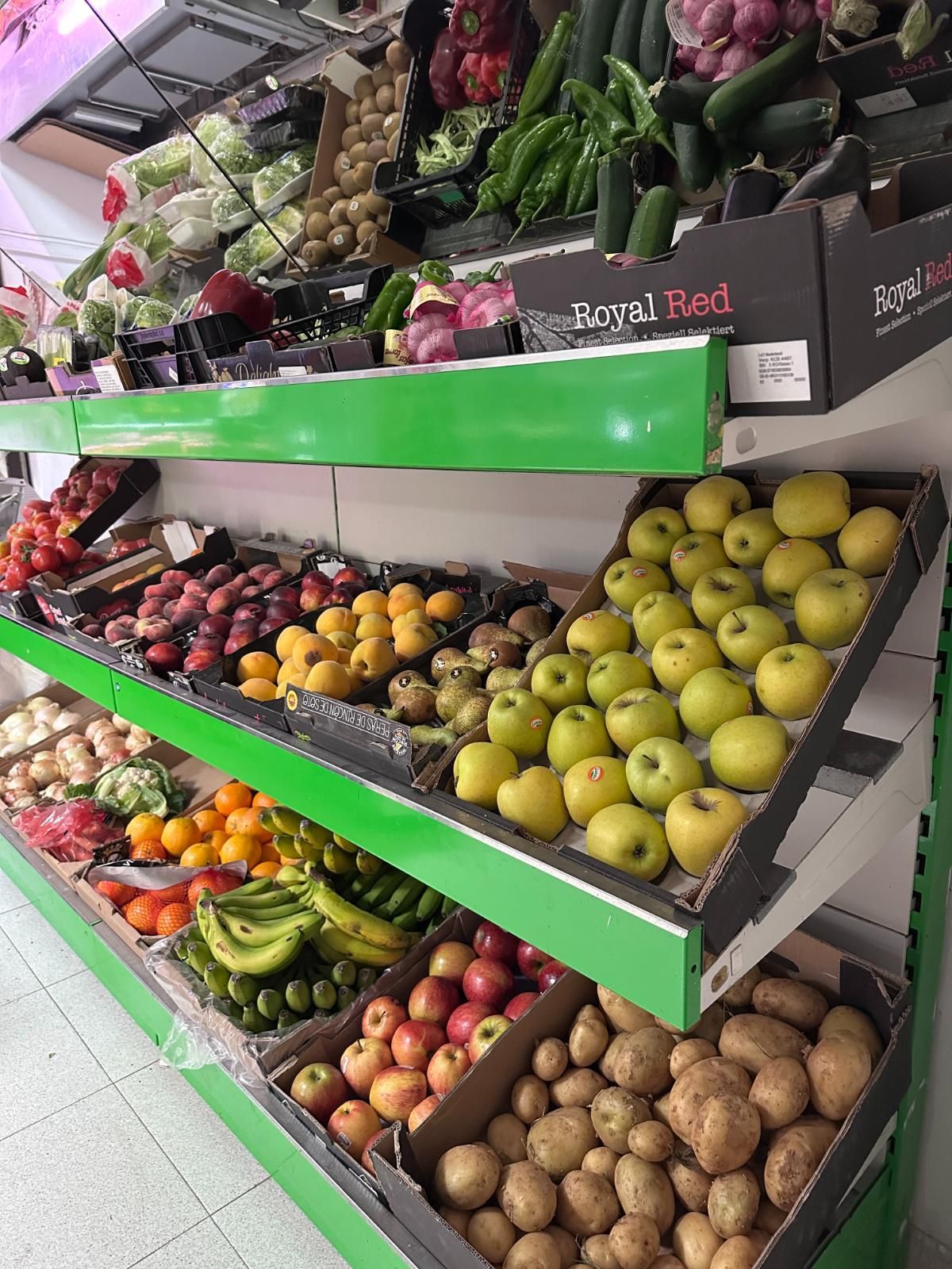 Estantes de productos frescos en un mercado: manzanas, patatas, tomates, pepinos y más en una tienda bien iluminada.