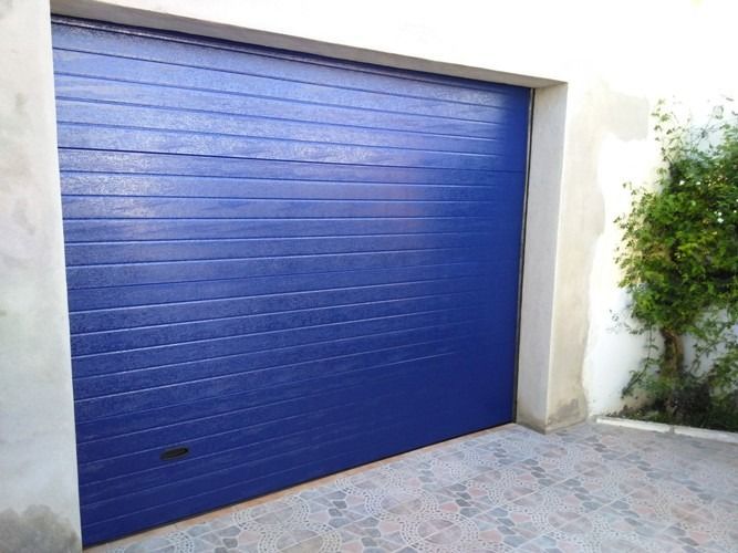 Una puerta de garaje azul con un árbol al fondo.