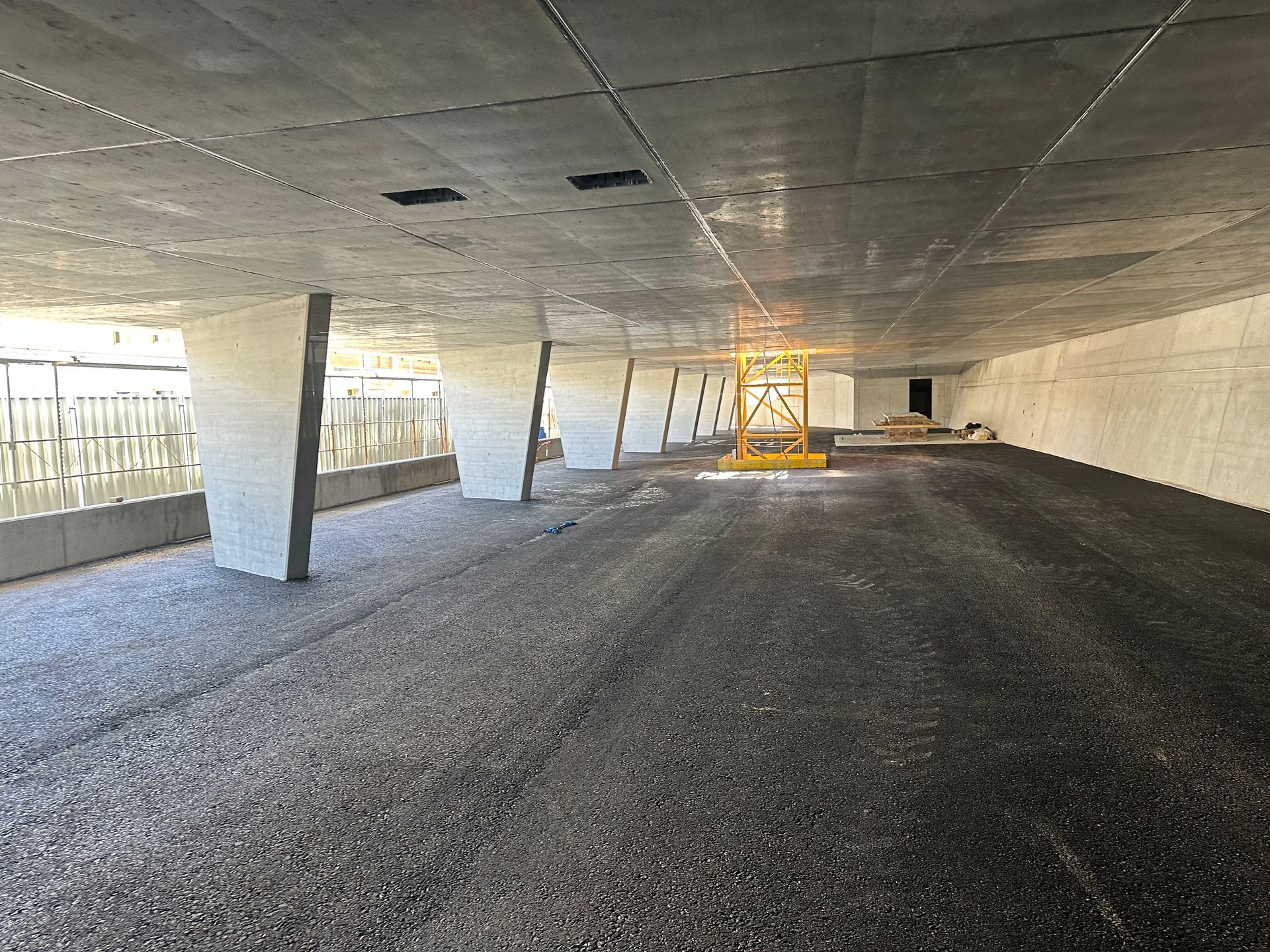 Un parking vide sous un pont avec un ascenseur jaune au milieu.