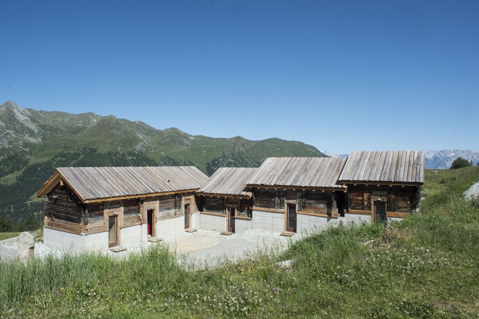 Un groupe de maisons en bois se trouve au sommet d'une colline herbeuse.