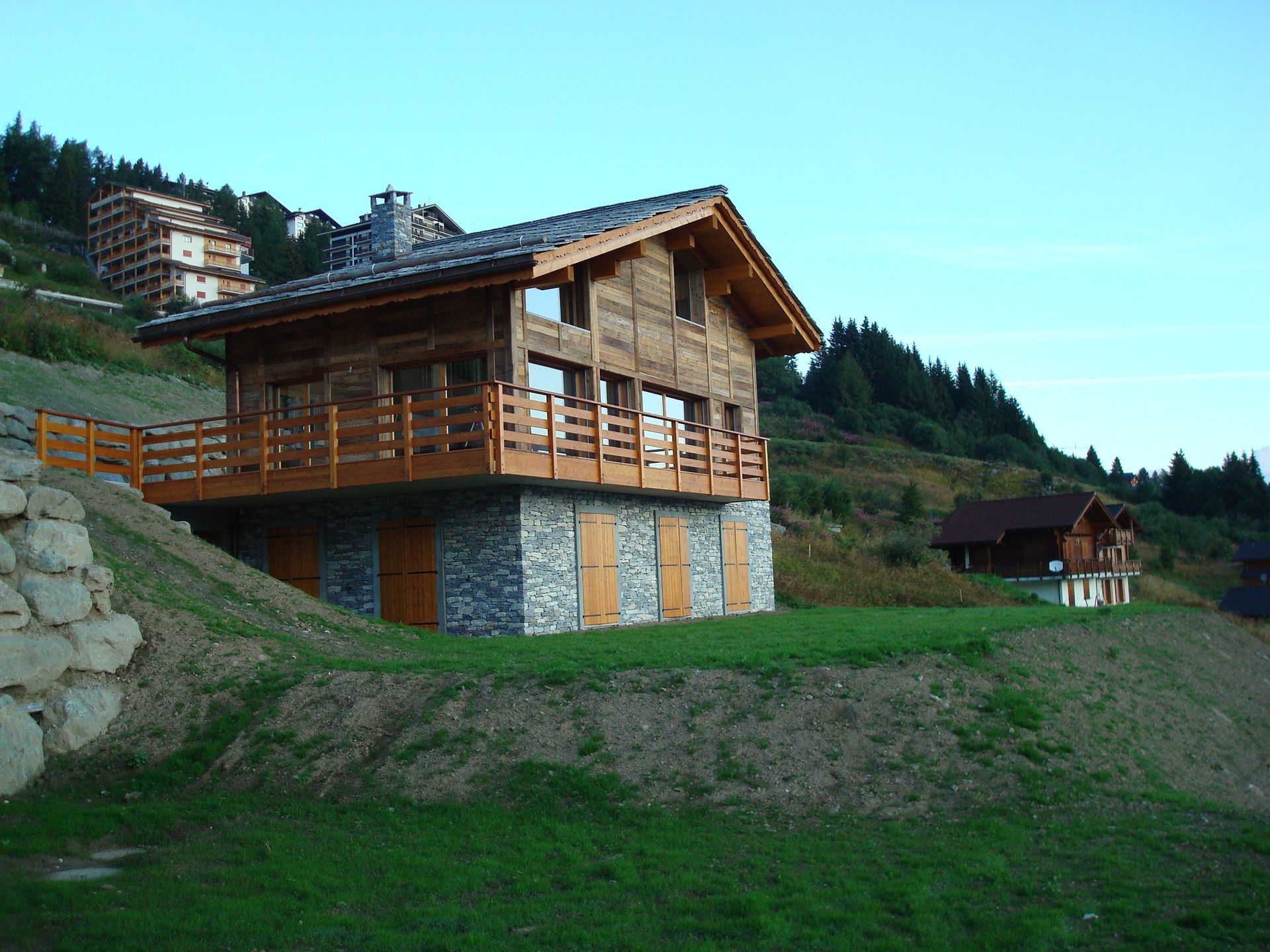 Une grande maison en bois se trouve au sommet d'une colline herbeuse