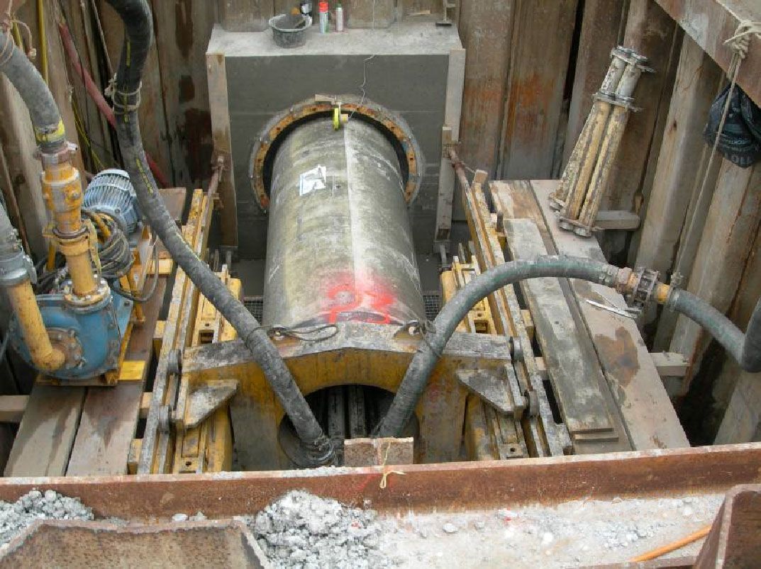 Un gros tuyau métallique est en train d'être foré dans le sol.