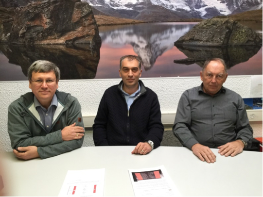 Trois hommes sont assis à une table devant un tableau de montagnes