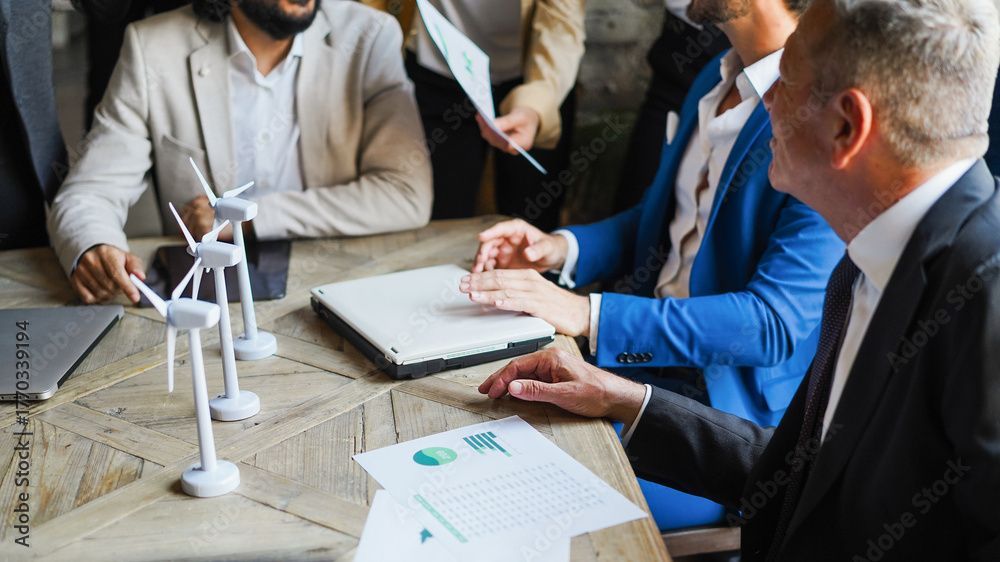 Geschäftsleute sitzen an einem Tisch mit Windkraftanlagenmodellen und besprechen Diagramme und einen Laptop.
