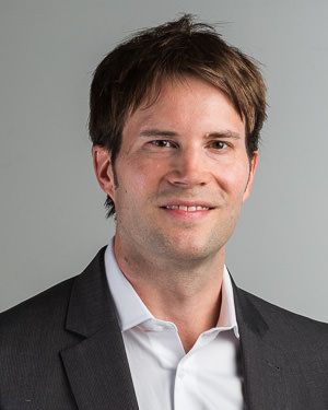 Zwei Personen in Anzügen analysieren an einem hellen Schreibtisch Daten auf einem Tablet und ausgedruckte Berichte.