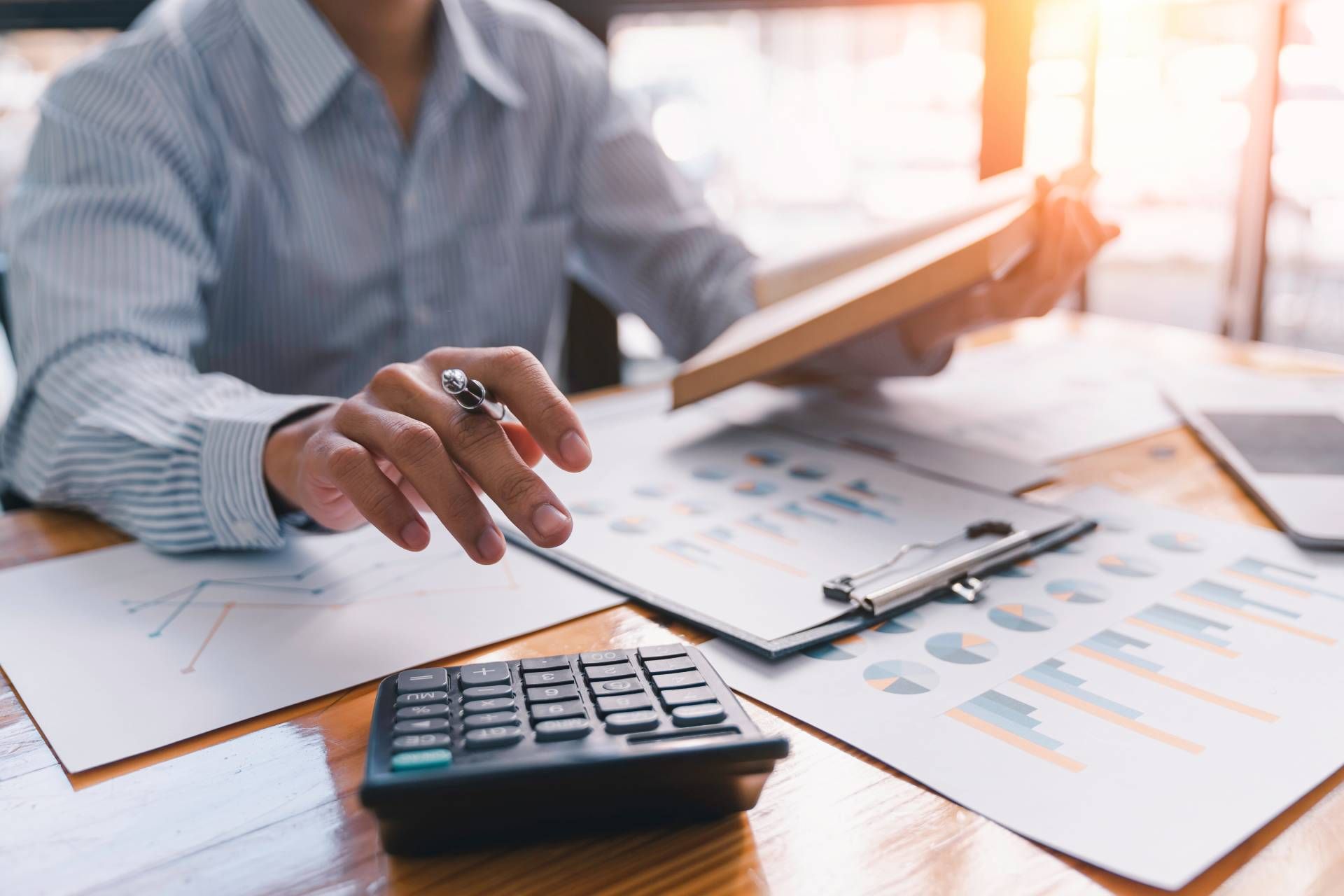 Eine Person prüft Finanzdokumente mithilfe eines Taschenrechners, Diagrammen und eines Stifts auf einem Schreibtisch.