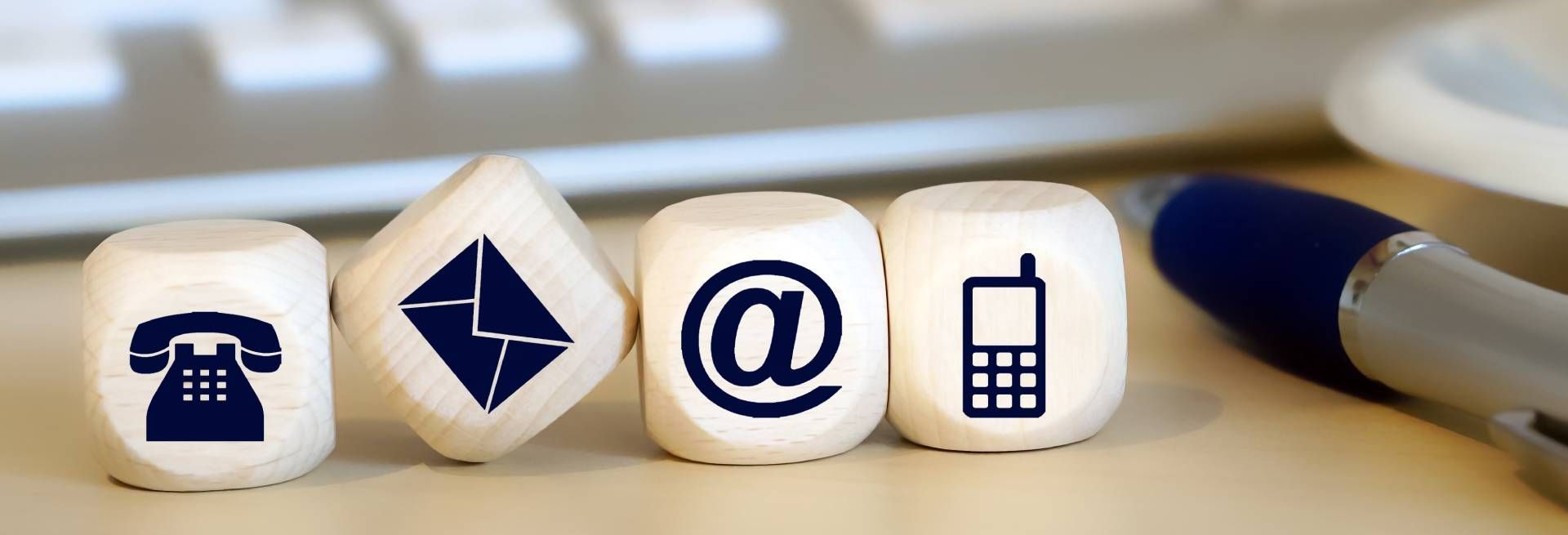 Kontaktinformationen: Telefon, E-Mail, Briefumschlag, Handy-Symbole auf weissen Würfeln. Ein Stift liegt daneben.