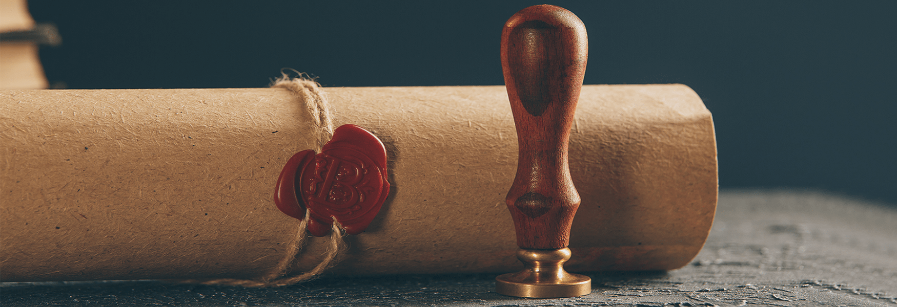 Pergaminho selado com cera vermelha e carimbo de madeira, sobre uma superfície cinza.